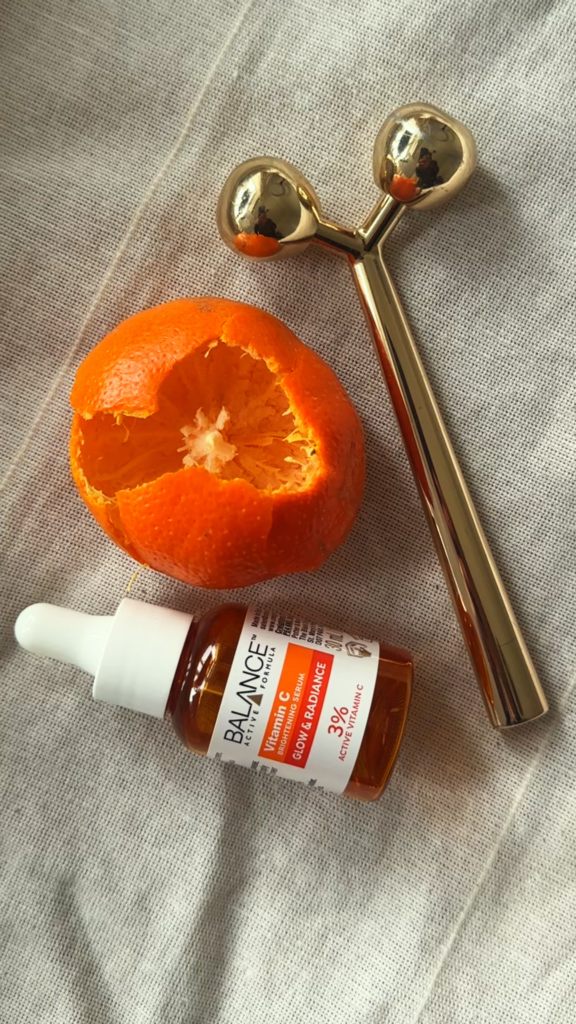 A close-up of a Vitamin C serum bottle beside a sliced orange on a neutral background, representing freshness and skincare vitality.